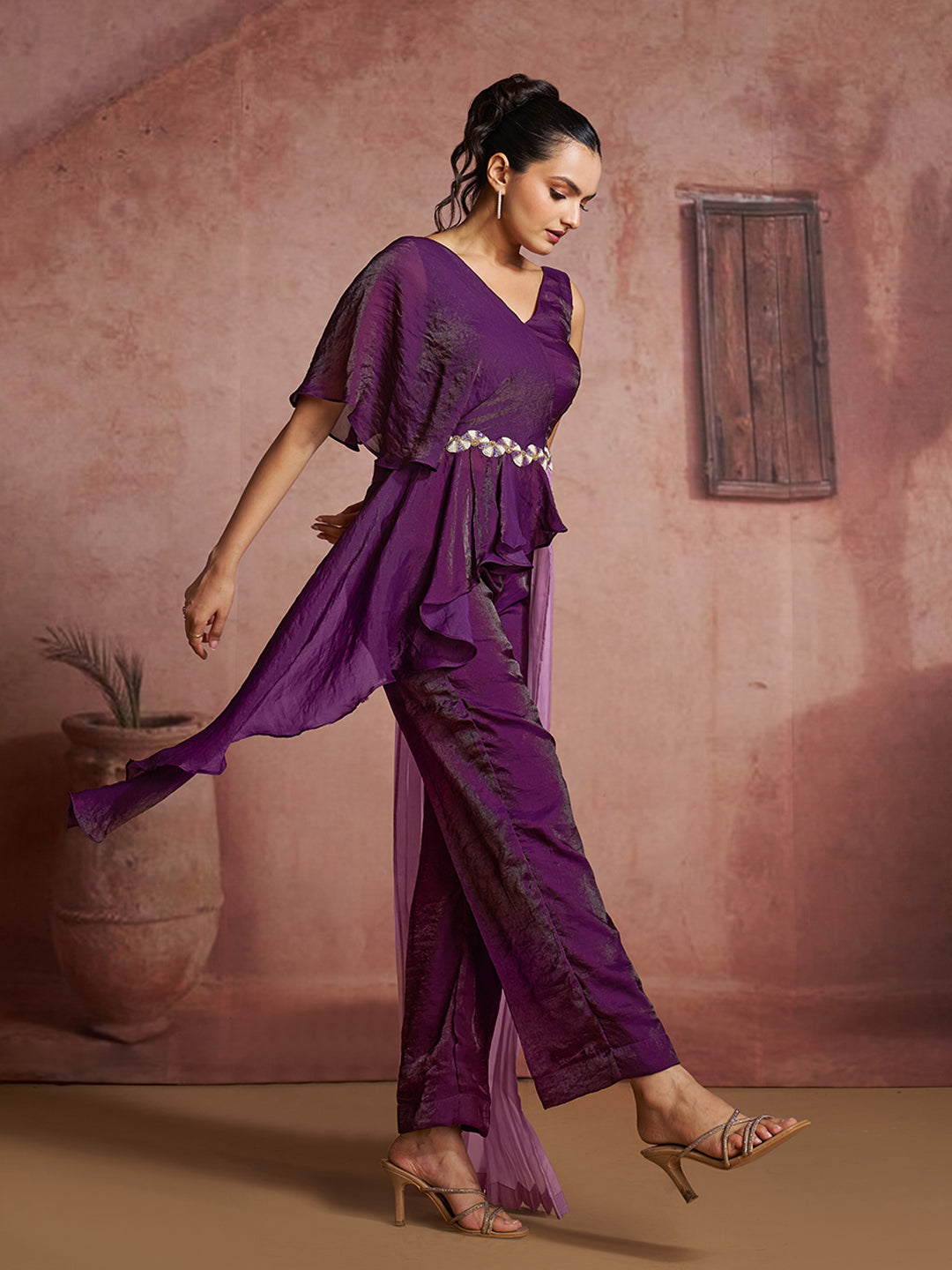 Elegant purple ruffled jumpsuit with a one-shoulder design and lavender pleated drape.